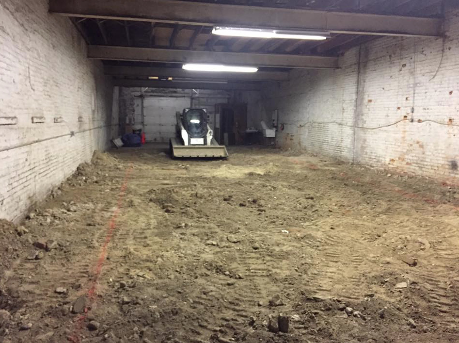an earth-mover sits motionless in a garage with a dirt floor